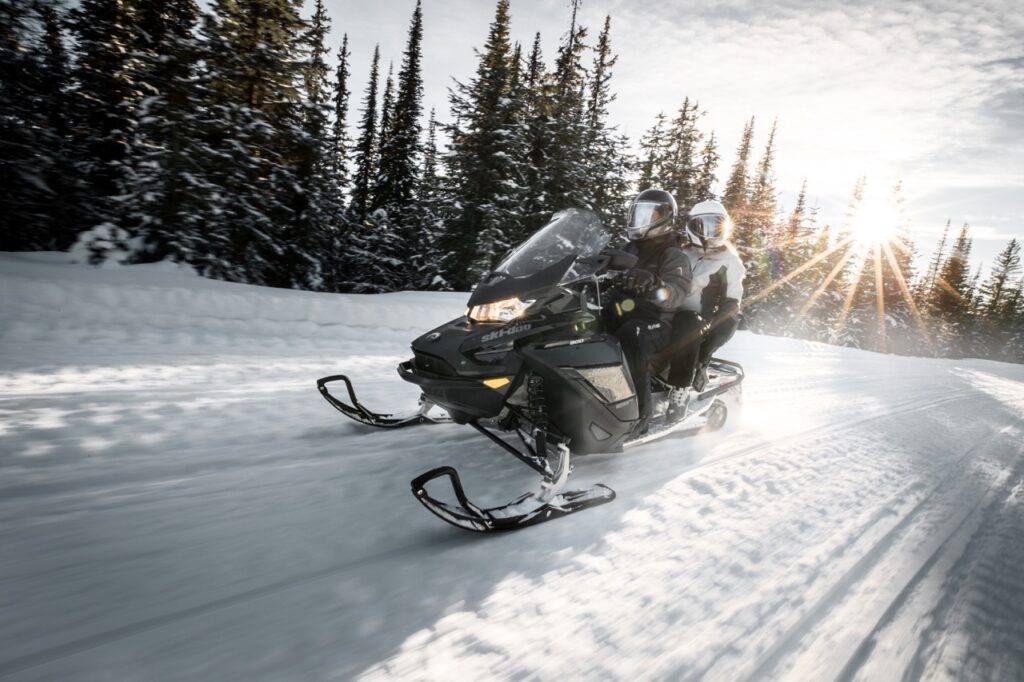 Couple riding double while wearing oxygen snowmobile helmets