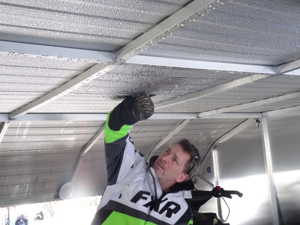 Loosening up ice layer with gloved fist inside helps prevent snowmobile trailer roof snow overload